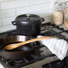 Black Staub five quart cast iron dutch oven on stove next to a cast iron pan