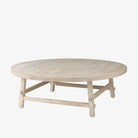 Whitewashed wood round coffee table with square dowel legs and bracing on a white background