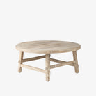 Whitewashed wood round coffee table with square dowel legs and bracing on a white background