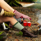 Woman pulling on striped alpaca socks outside by a fire 