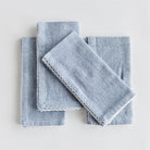 Set of four blue dinner napkins with white scallop trim on a white background