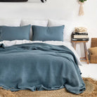 Waffle Weave Bed Blanket in Slate Gray Blue on a bed with white sheets in a room with white walls and a jute rug