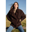 Model sitting on a fence in front of a field wearing jeans and Z Supply Ari Sherpa Coat in Dark Chocolate