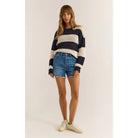 Model wearing Z Supply Broadbeach Stripe Sweater in Captain Navy with cut off jean shorts and white sneakers