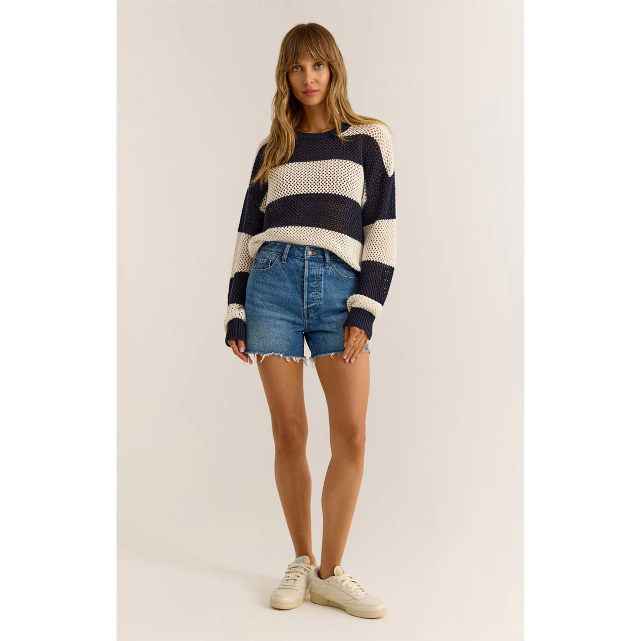 Model wearing Z Supply Broadbeach Stripe Sweater in Captain Navy with cut off jean shorts and white sneakers