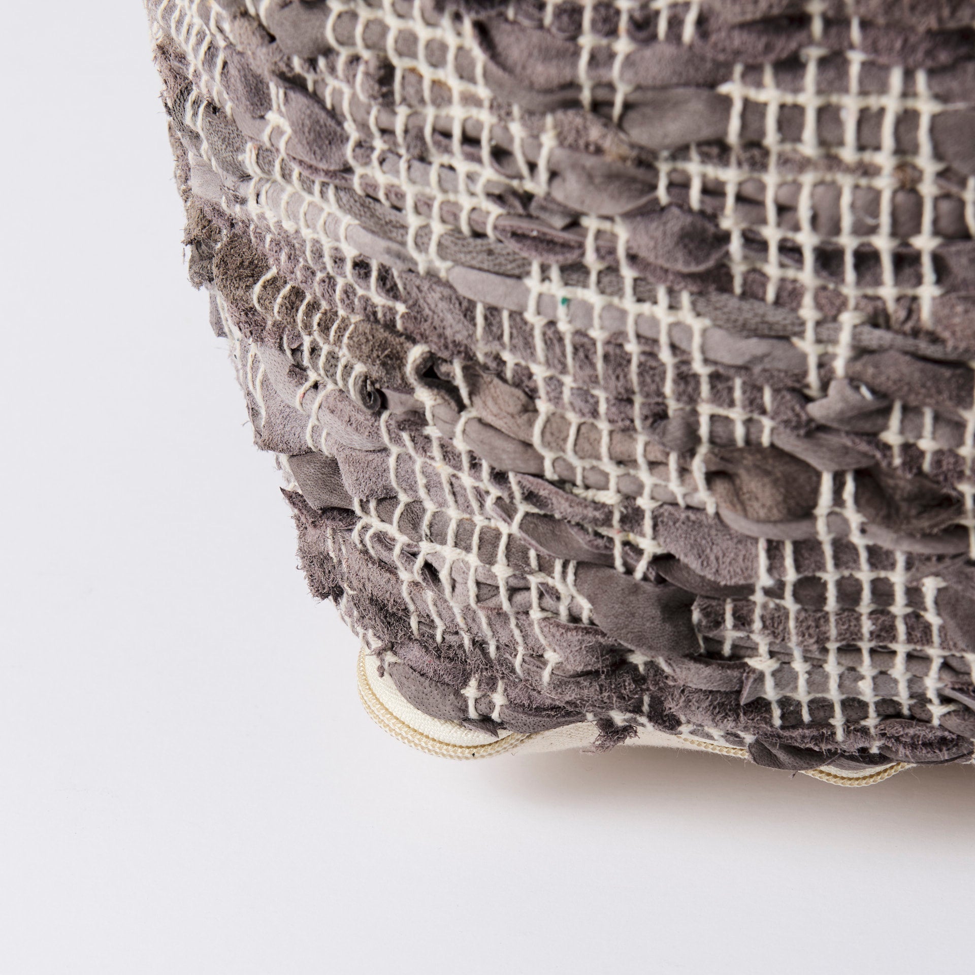 Close up of Grey square pouf with cotton and leather accents in geometric pattern on a white background