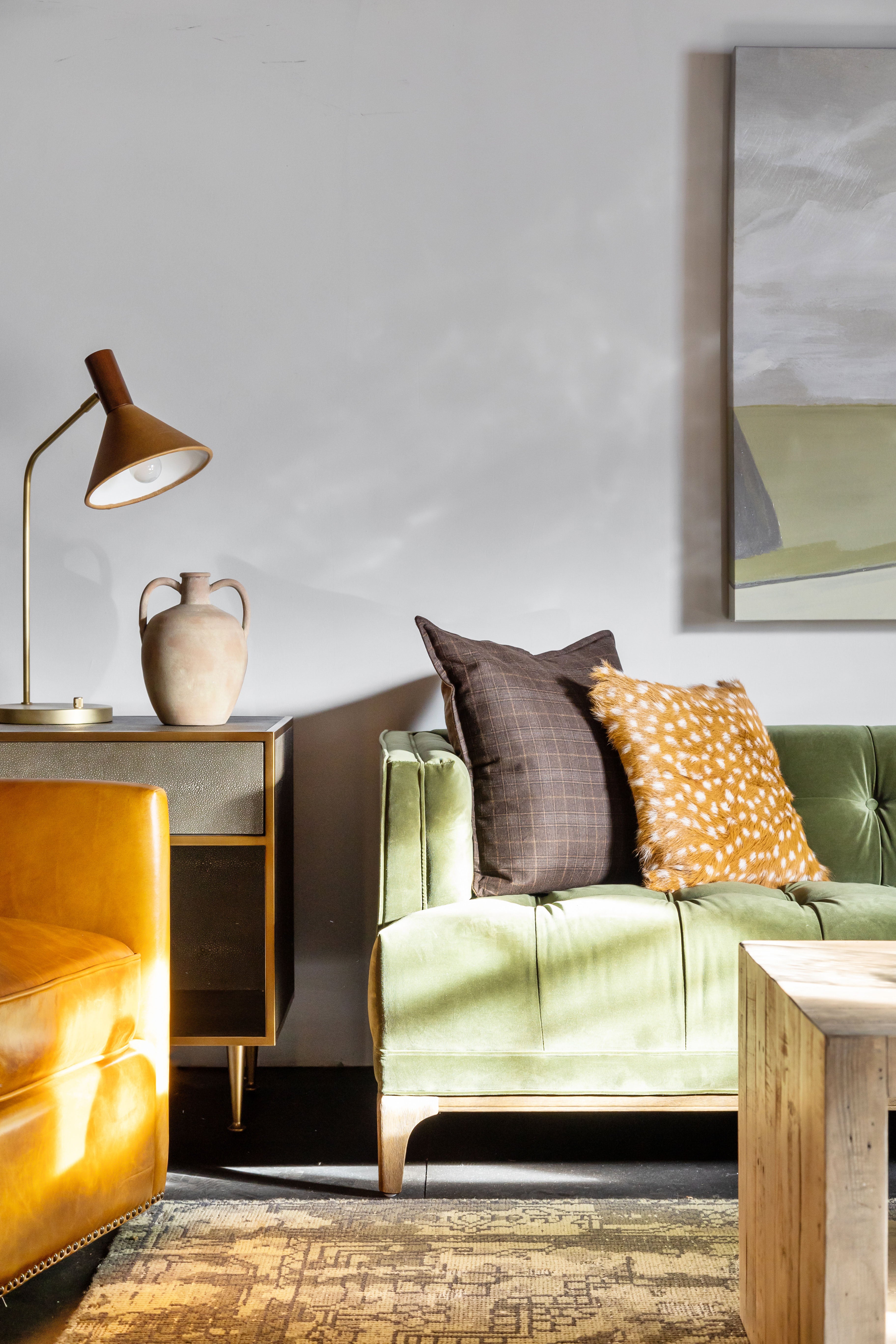 Living room area with Four hands brand green velvet Dylan sofa with paintingw with wood coffee table in front and leather armchair 