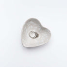 Close up of Decorative white stoneware heart dish on a white background with rings inside