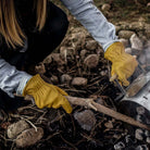 Woman bending down in garden with soil and stick wearing Pair of Yellow leather garden work gloves 