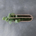 Long rattan basket with green and white flowers on a stone surface