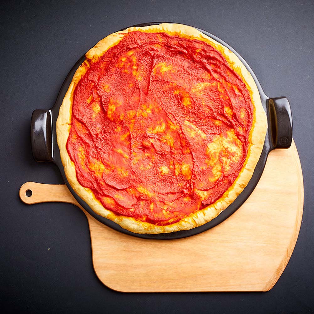 Emile Henri brand pizza peel with pizza on top of Beechwood pizza peel on a black background