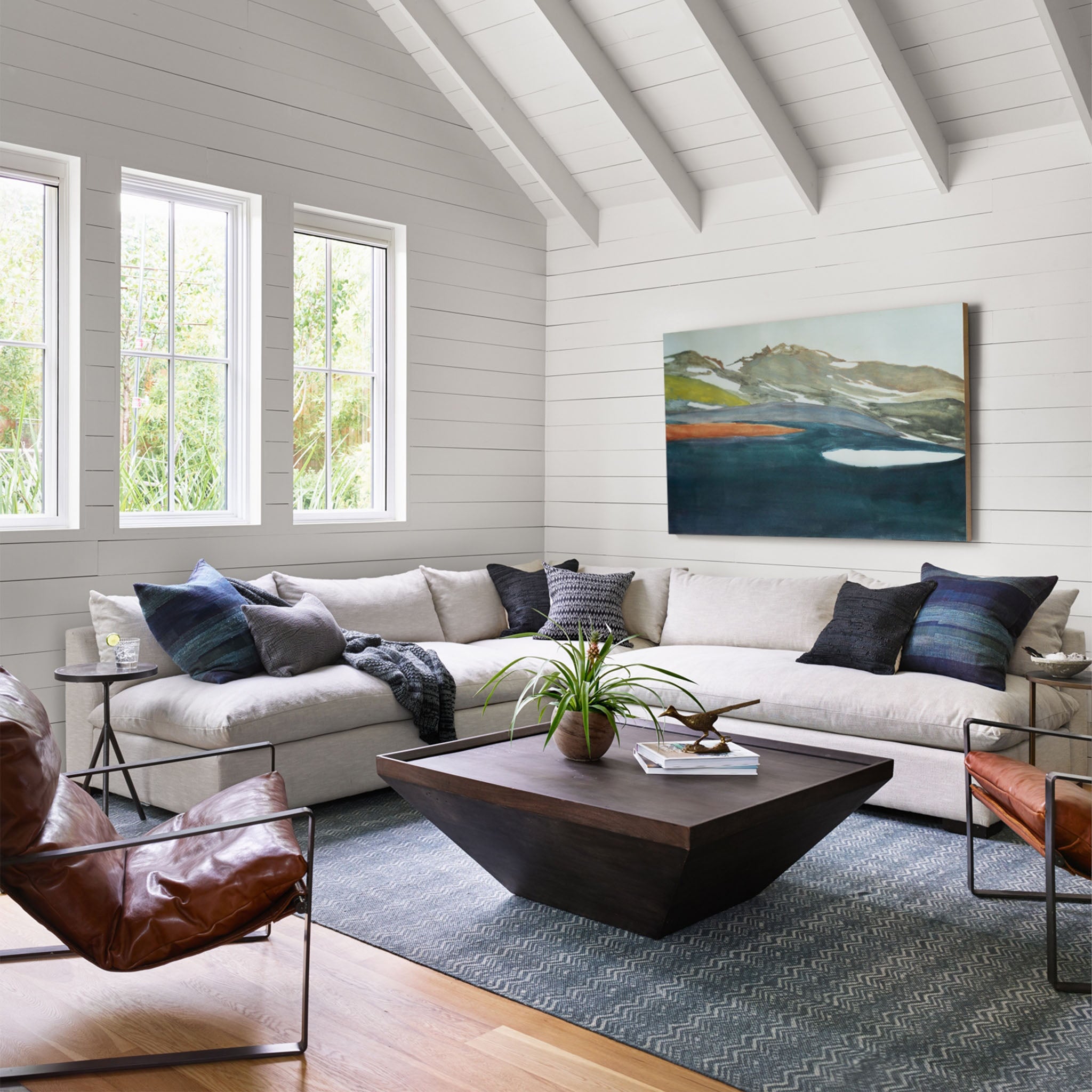 White living room with vaulted celling and big white sofa and two Tobacco brown leather 'Emmett' sling chairs by Four hands furniture with iron frame