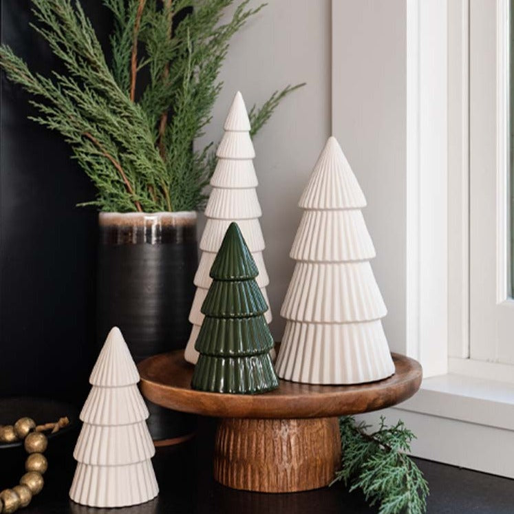 Ceramic decorative christmas trees in white and green on a wood tray with greenery