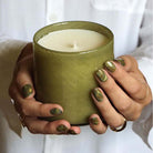 Lafco brand 'sage and walnut' green glass candle held by a woman with white shirt and green painted nails