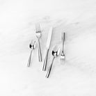 Stainless flatware five piece set with simple lines and polished finish on a marble surface