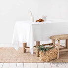 White linen table cloth on a wood table in room with white walls and seagrass rug