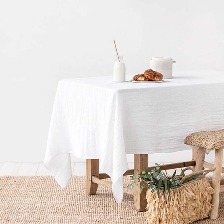 White linen table cloth on a wood table in room with white walls and seagrass rug