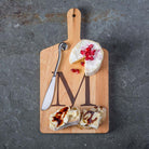 Monogrammed maple cheese board with letter 'M' engraved with cheese and stainless cheese knife on a black counter