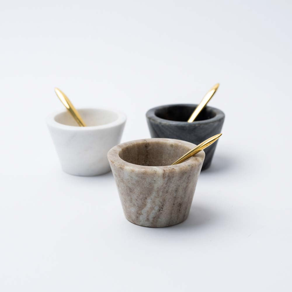 Set of three small marble bowls with brass spoons on a white background