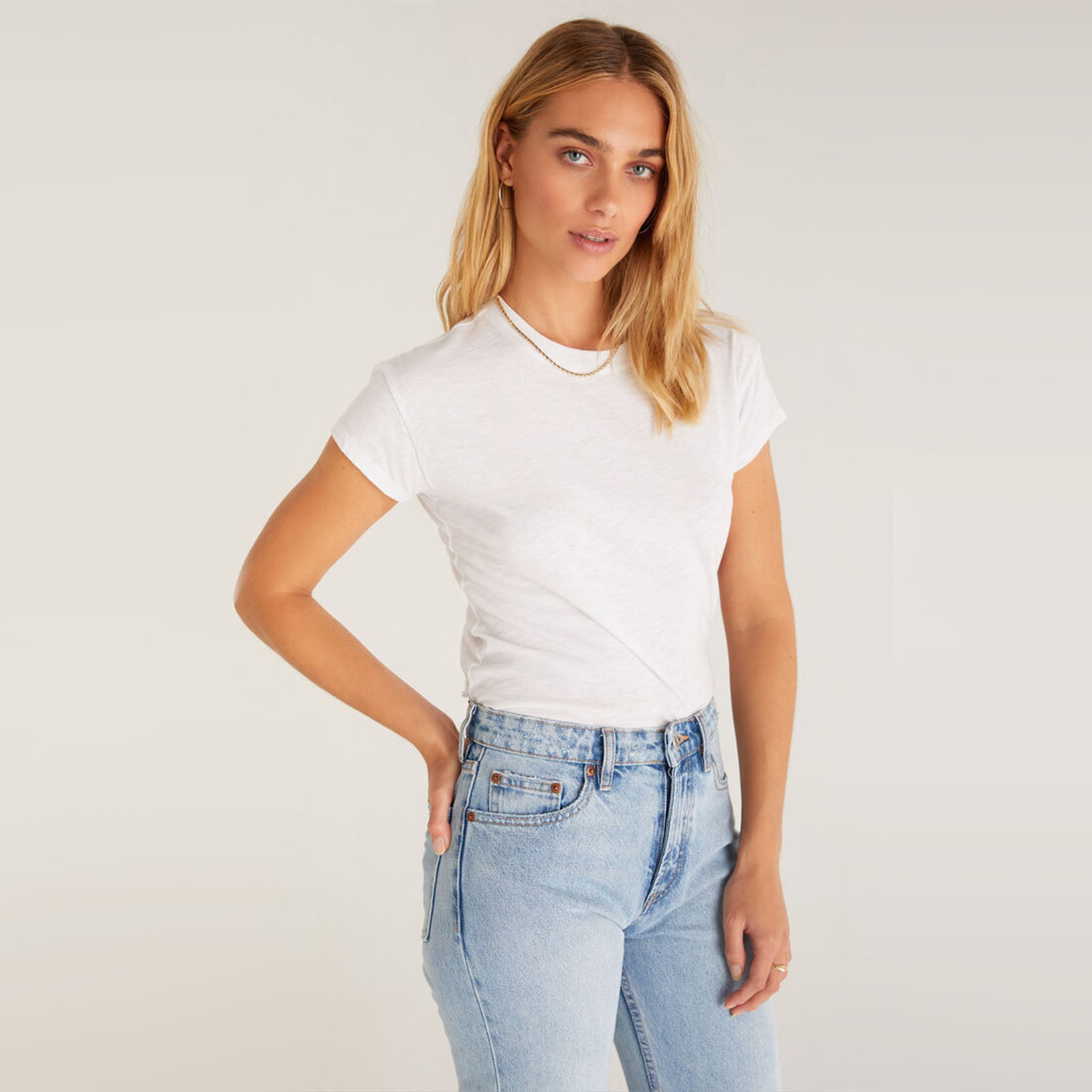 Model wearing jeans and Z supply modern slub white t shirt in front of a white background