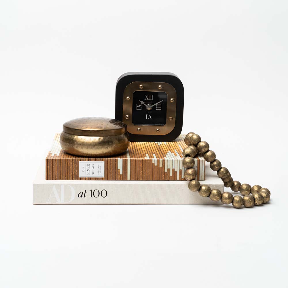 Black and gold table clock on a stack of books with accessories on a white background