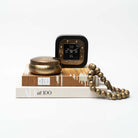 Black and gold table clock on a stack of books with accessories on a white background